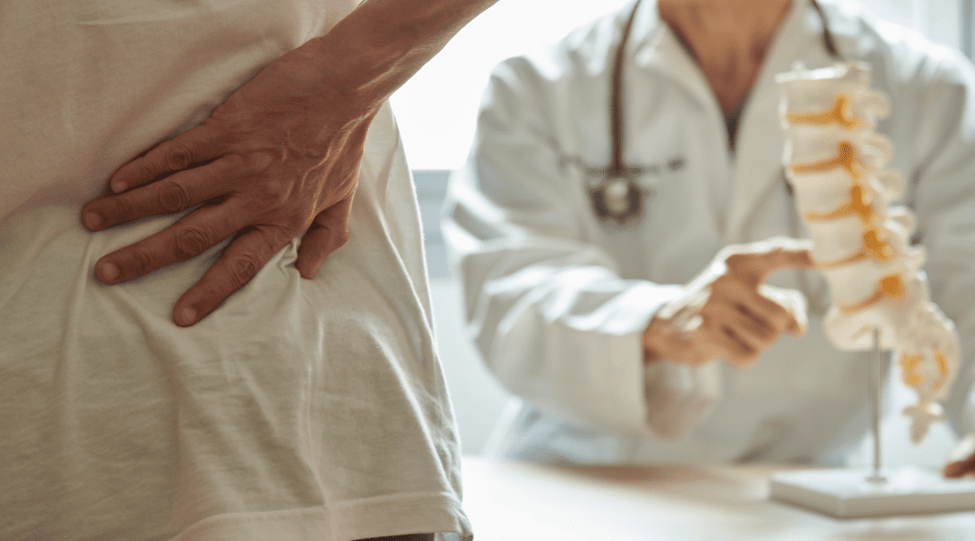 A male doctor explaining lumbar anatomy to female patient complaining of back pain at medical clinic